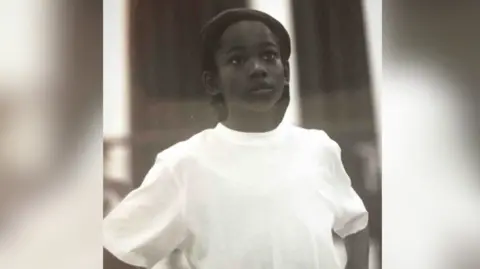 Young boy in white t-shirt looks upwards away from the camera. The photo is black and white.