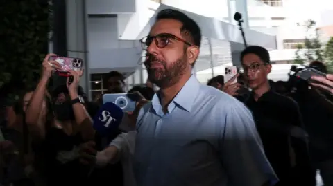 Side view of Pritam Singh arriving at the court, surrounded by reporters