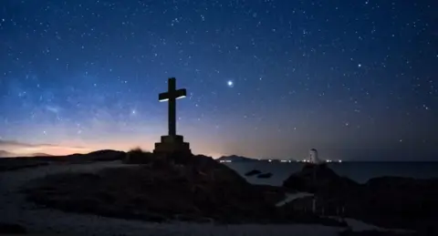 Mathew Browne A cross silhouetted in the darkness
