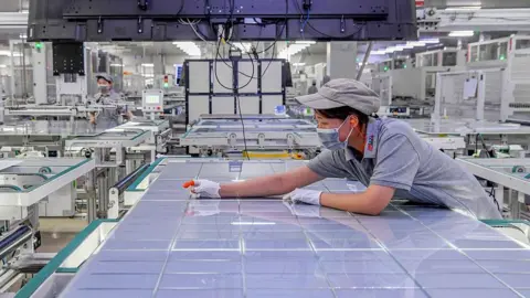 A woman leans over a large sheet of solar panel modules at a factory in Jinhua, Zhejiang Province of China. 