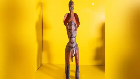 Manchester Museum handout A carved wood figure of a horse with an ibis on its back on display with a yellow background.