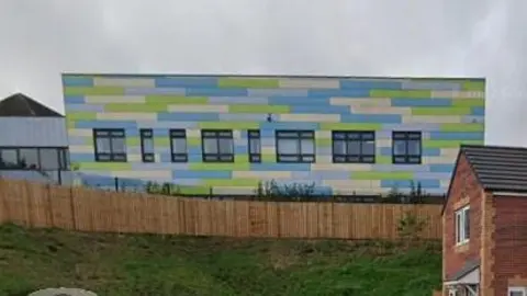 LDRS A school building with blue and green cladding seen from behind a wooden fence.