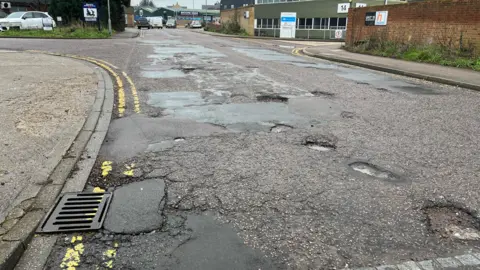 Tony Fisher/BBC A road with lots of potholes and double yellow lines on both sides. The road is on an industrial estate.