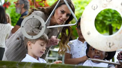 PA Media Catherine plays with objects suspended in the air in the garden of a primary school alongside pupils.