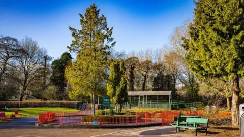 LDRS Ground level view of a typical city park, with a number of mature trees among lawn areas and a small pavilion