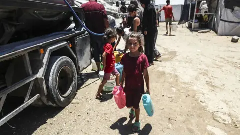 Getty Images A child carries a cans filled with water while an aid truck distributes water to displaced Palestinians amid a worsening water crisis in Gaza City, Gaza on 7 July 2025.