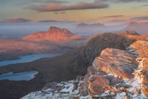 Jeremy Morris Red tinged sunlight over a rocky and mountainous landscape.