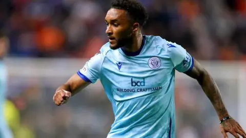 PA Media a footballer wearing a light blue kit with his arms outstretched during a match