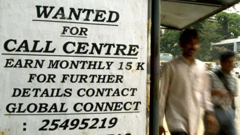 Getty Images People walk past an advertisement for BPO work paying 14,000 rupees a month.