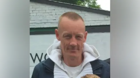 Family handout A man with short hair and one gold earring, wearing a white hoodie and navy coat, smiles at the camera.