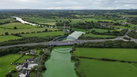 Colleen Webb Drone shot showing green fields in Toome with bright green river flowing through it