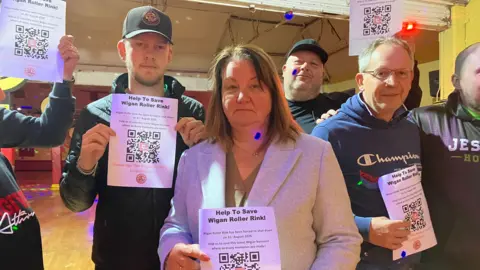 Dawn Holding holding a piece of paper reading: 'Help to save Wigan Roller Rink' with others.