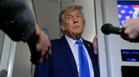 Trump wears a blue tie and pokes his head through a door on Air Force One to speak to reporters while returning from G7 meetings in Canada.
