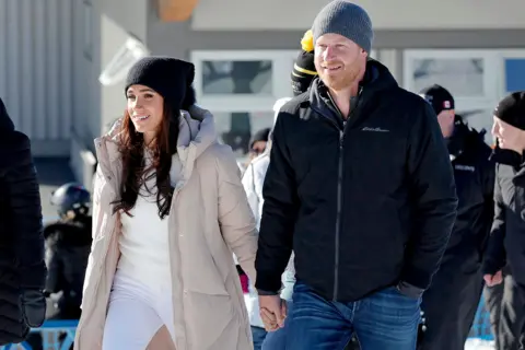 Getty Images Meghan and Prince Harry, wrapped in winter clothing and holding hands, at an 2024 outdoor event in Vancouver for the Invictus Games