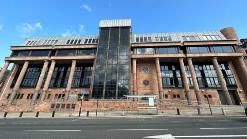 A large court building, it has red bricks and columns and large dark windows.