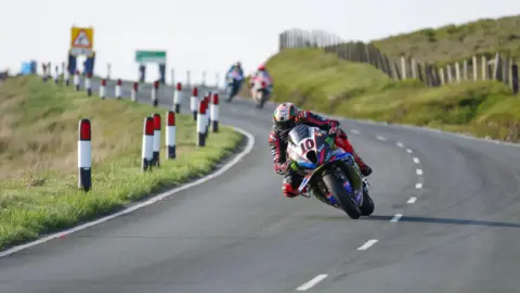 IOM TT A racer with a number 10 plate on the front of his bike on a section of the Mountain Road, with two other riders following behind.