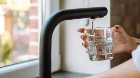 A hand holding a glass under a running tap.
