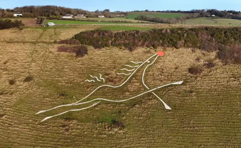 Gareth Fuller/PA Media A presumption    of the White Horse, carved into Cheriton Hill, adjacent   Folkestone, Kent,  but with a circular  reddish  nose, depicting the legendary Rudolph, the red-nosed reindeer.
