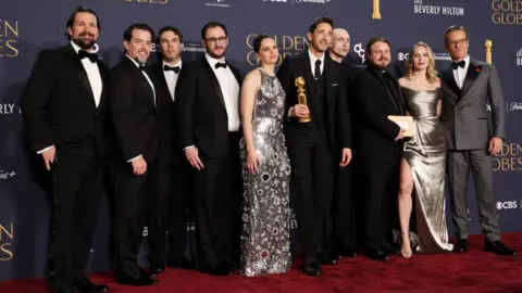 Getty Images Trevor Matthews, Brian Young, Felicity Jones, Adrien Brody, winner of the Best Performance by a Male Actor in a Motion Picture – Drama Award for "The Brutalist," Daniel Blumberg, Brady Corbet, Mona Fastvold, and Guy Pearce pose in the press room during the 82nd Annual Golden Globe Awards at The Beverly Hilton on January 05, 2025 in Beverly Hills, California.