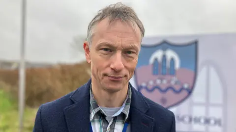 Man wearing a blue jacket and checked shirt smiling at the camera 