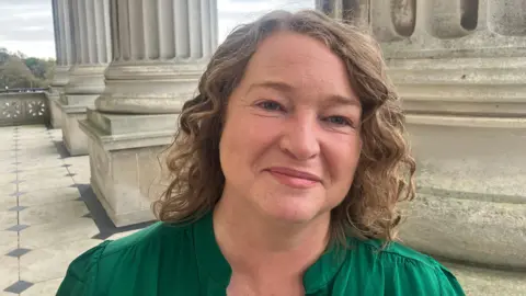 Phyllis Stephenson wears a green shirt and has brown curly hair. 