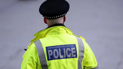 PA Media A police officer facing away from the camera wears a yellow high-vis jacket and a flat black police hat.