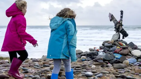 Children look at a memorial for Dobby, a fictional house elf from the Harry Potter fantasy novels and films, at Freshwater West beach on November 6, 2022 in Castlemartin, United Kingdom. 