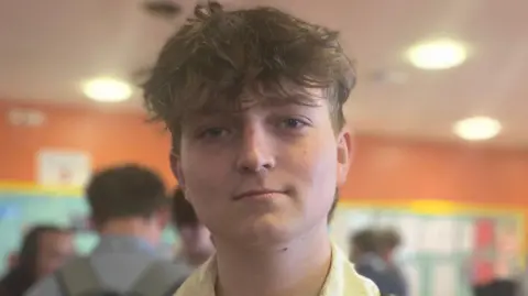 A boy with messy brown hair looking towards the camera.