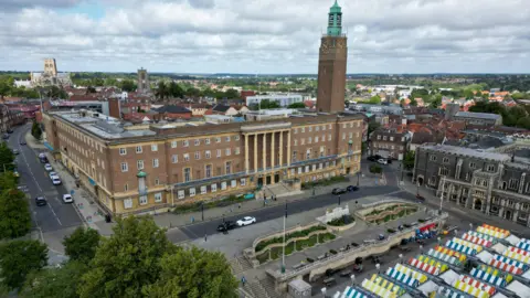 Martin Barber/BBC Norwich's 1930s City Hall building, with its clock tower, can be seen and colourful market stalls can be seen in the front.