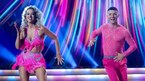 Woman and man both in pink outfits dancing 