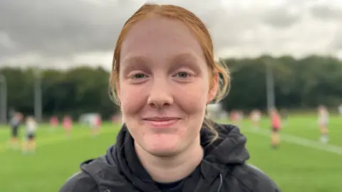 A girl with her hair in a pony tail, smiling at the camera at the training ground in a black Hull City Ladies hoodie