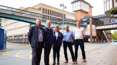 Shropshire Council Four men and one woman standing in front of a footbridge and a car park. 