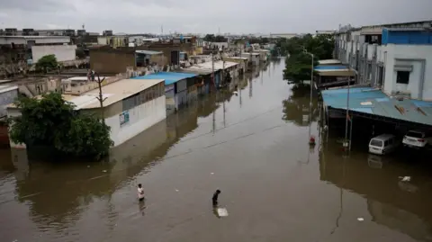 Reuters La gente cruza una calle inundada tras las fuertes lluvias en Ahmedabad, India, el 28 de agosto de 2024