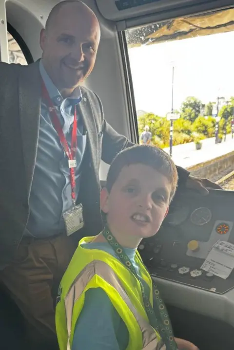 Transpennine Express Nathaniel, in a high visibility vest, in the cab of a train with Steve Whitehead.