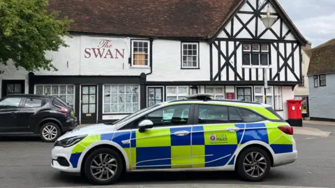 Lewis Adams/BBC A police car parked in front of a large pub that has a black and white exterior.