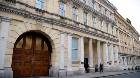 Getty Images Facade of the court with large brown wooden entrance gate to one side and columns at the entrance of the sand-coloured building with tall sash windows