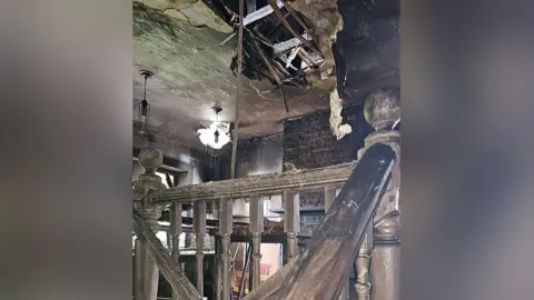 Claire Hannah Images shows inside a historic pub after a fire - from the top of the stairs on the first floor. It shows damage to the wooden banister and gaps in the roof caused by the blaze.