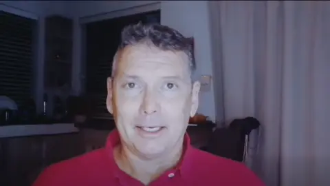 Ian von Memerty looks into the camera, wearing a red shirt