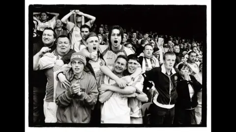 Black and white photograph of Torquay United fans in the away end at Southend United, with anguish on their faces, moments before they are promoted to the old Second Division in 2004.
