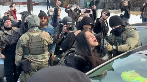 ICE officers pull a woman away from a car.