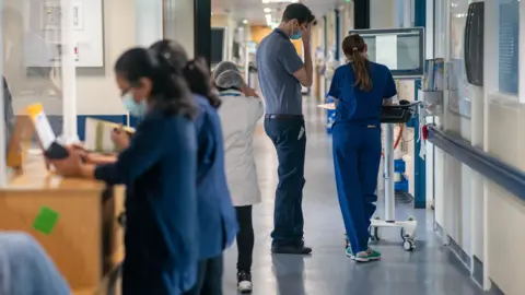 A hospital corridor with nurses and a doctor standing at work stations.