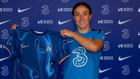 Lucy Bronze holds up a Chelsea shirt