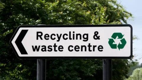 A black and white road sign, which reads 'recycling and waste centre'