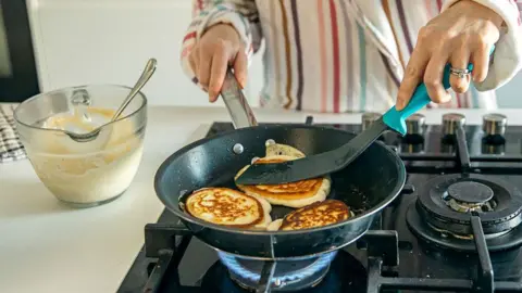 Woman cooking pancakes in a frying pan on a gas hob