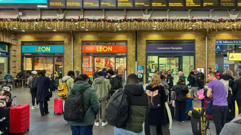 Getty Images A crowd of people stand under train departure boards at Kings Cross station, which have been decorated with Christmas lights.
