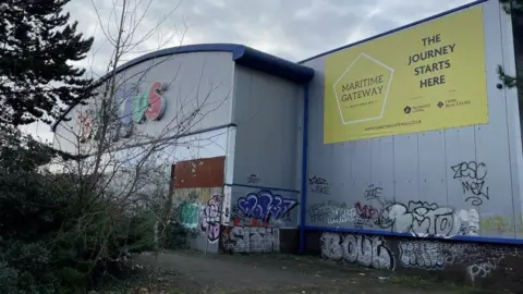 The outside of an old Toys R Us building covering in graffiti and overgrown bushes