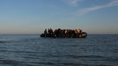 Reuters Black inflatable dinghy in the English Channel. It is filled with people. 