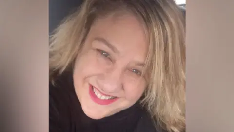 Facebook A selfie of Sarah Forrester. She is smiling at the camera and has pink lipstick on. She has shoulder-length, blonde hair and is wearing a black top.