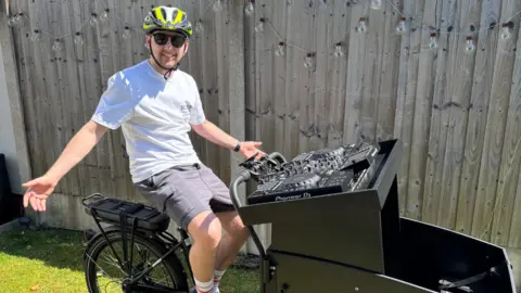 A man sitting on a bike with a DJ deck on the front of the bike. 