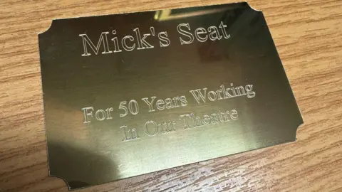 Everyone Active A decorative gold plaque that says "Mick's Seat For 50 years working in our theatre'